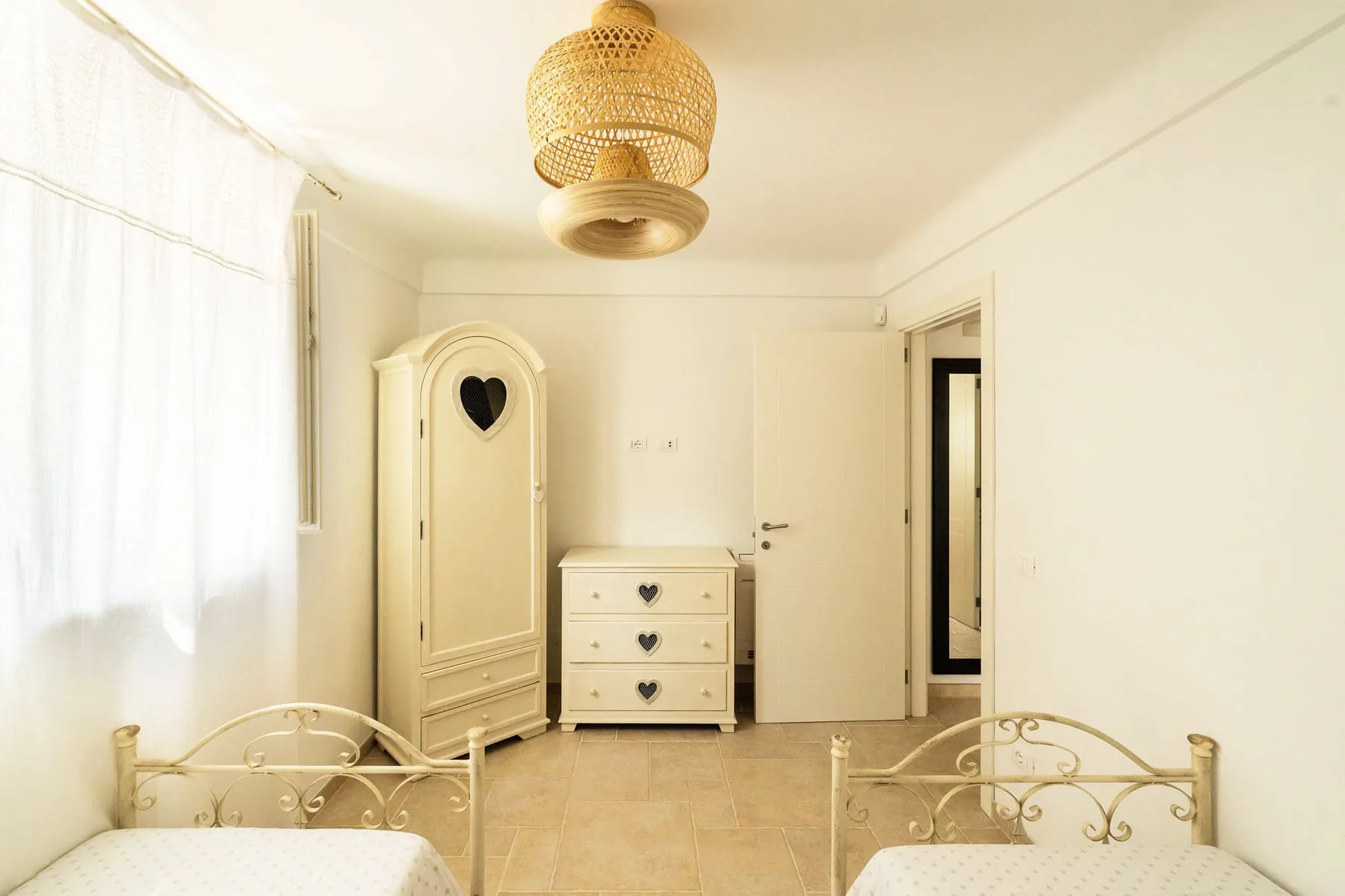 A bright bedroom with two beds and a cream-colored wardrobe.