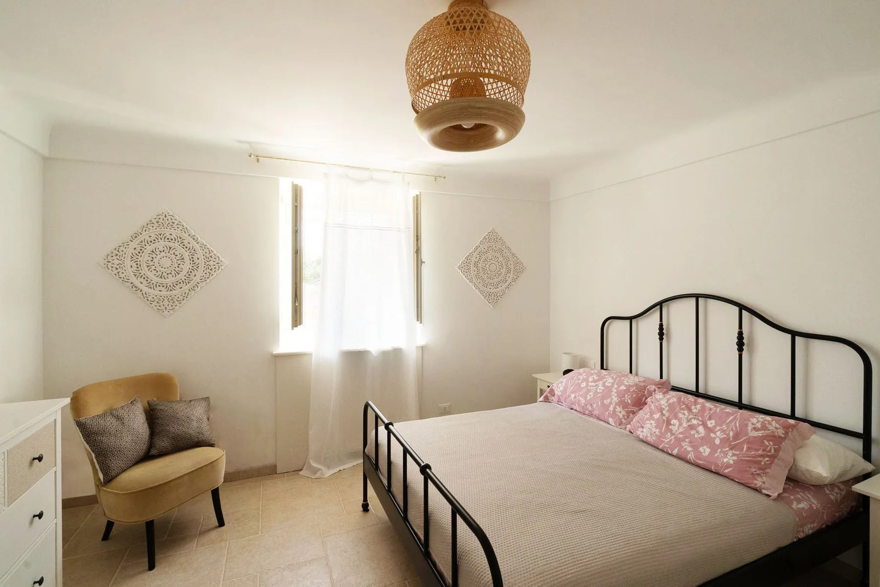 A bright bedroom with a metal bed, window, and seating.