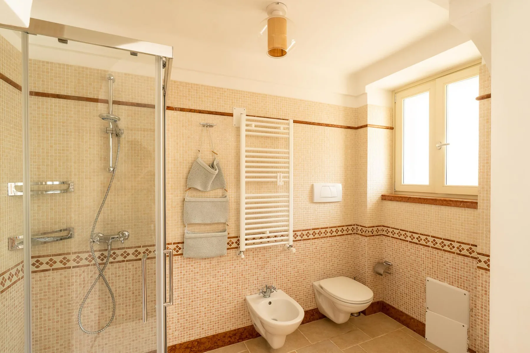 A tiled bathroom with a shower, sink, toilet, and wall-mounted towel warmer.