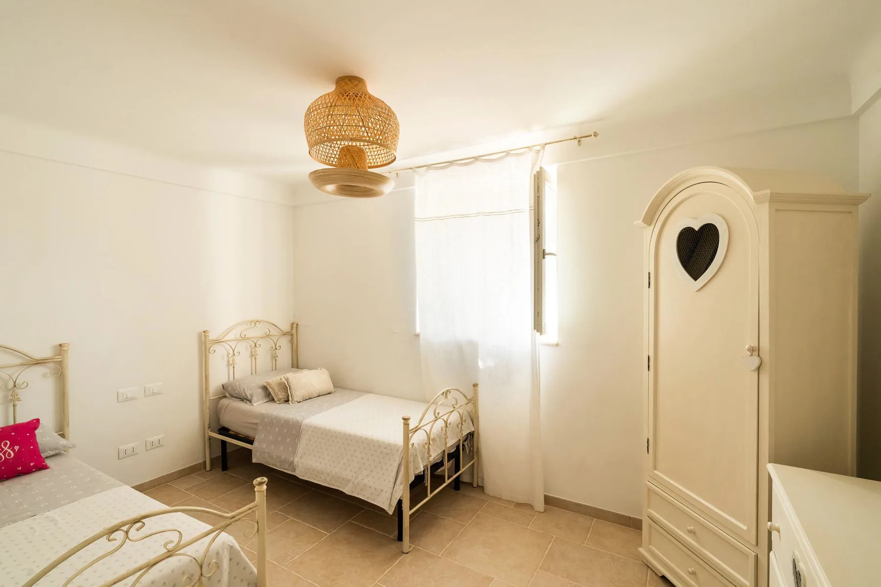 A bright bedroom with single beds, a wardrobe, and a woven pendant light.