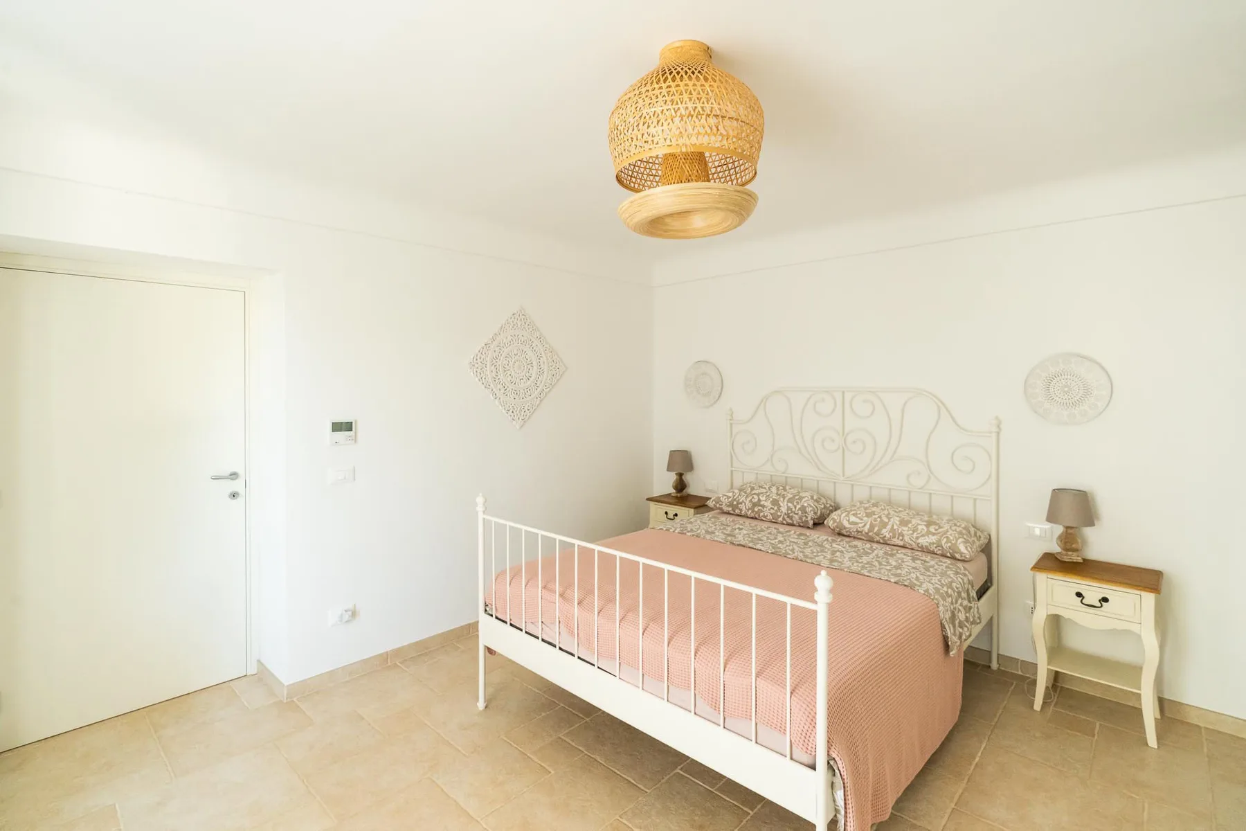 A bright bedroom with a white bed, pink bedding, and matching bedside tables.