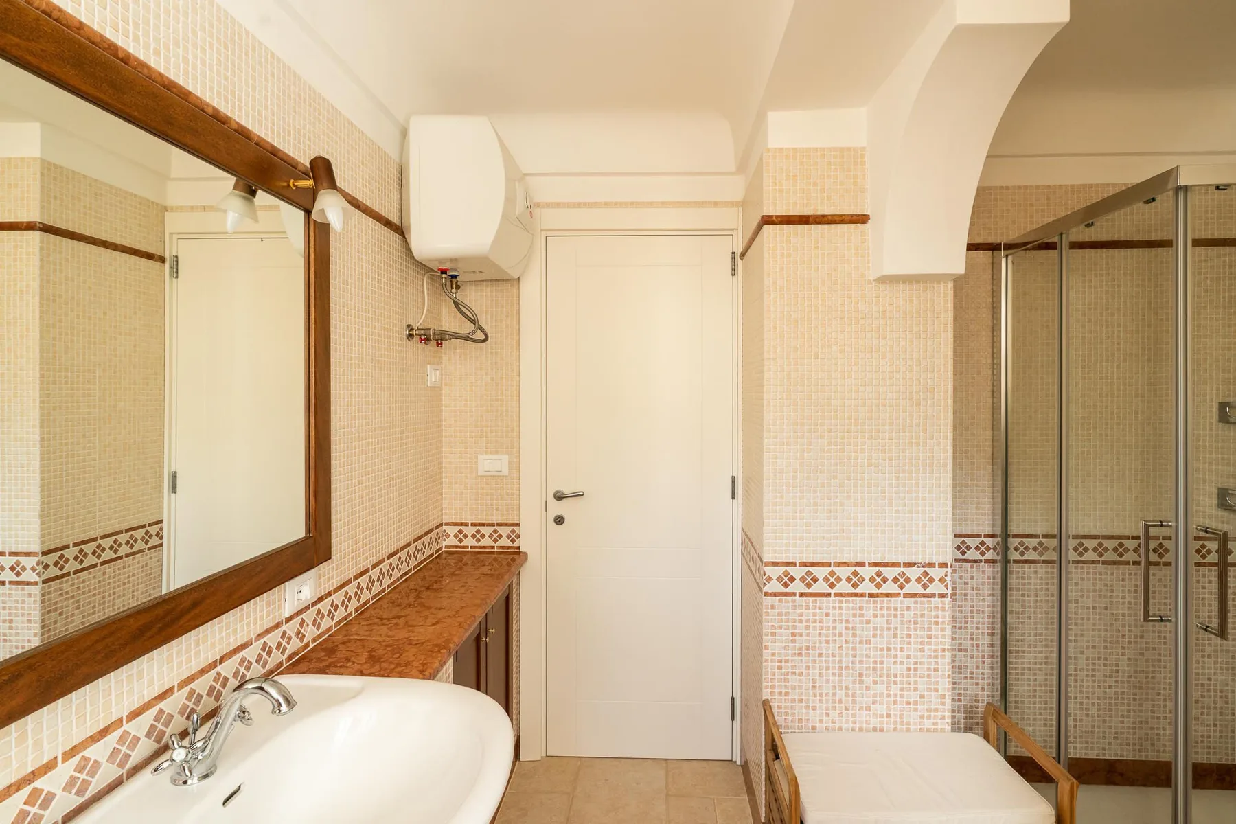 A tiled bathroom with a sink, mirror, and glass shower enclosure.