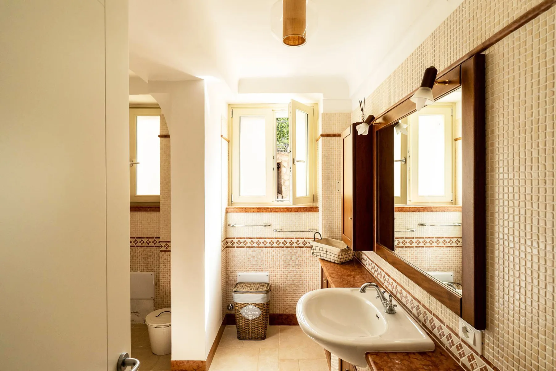 A tiled bathroom with a sink, mirror, and bright window.
