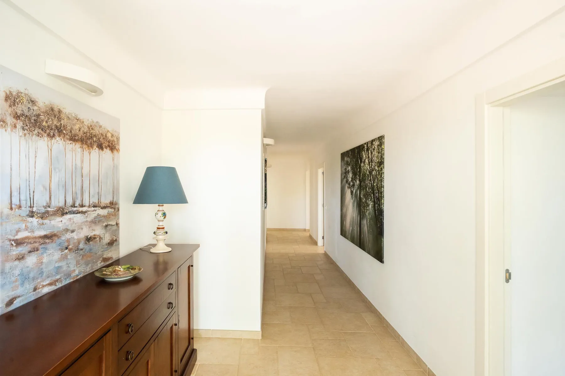 A bright hallway with tiled flooring and artwork along the walls.