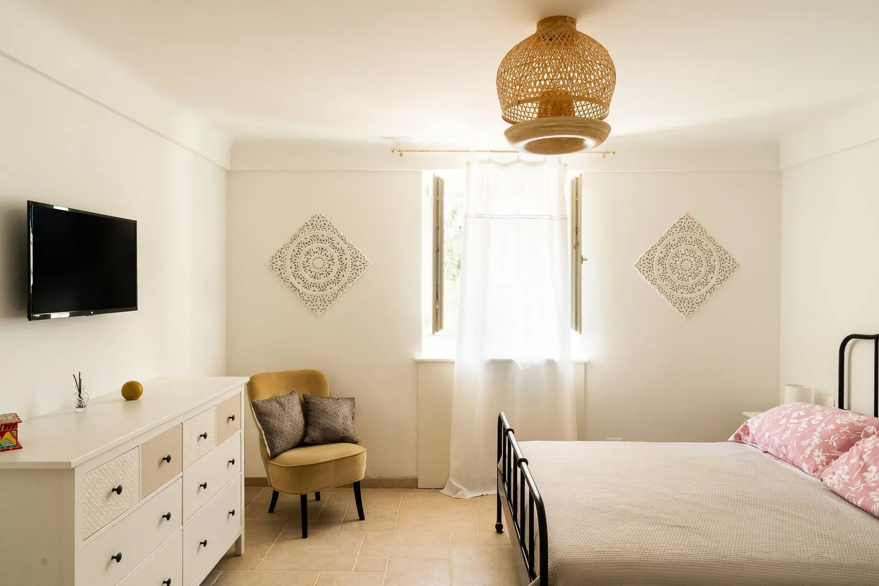 A bright bedroom with a bed, a dresser, and a window with sheer curtains.