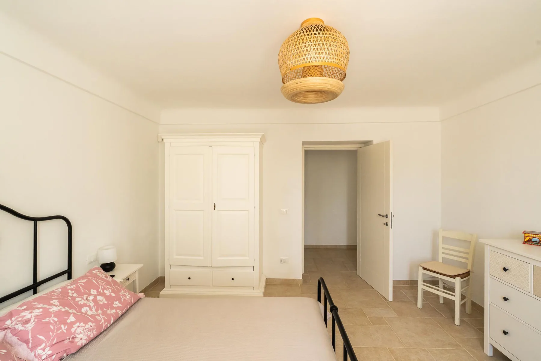 A bright bedroom with a bed, a wardrobe, and an open doorway.