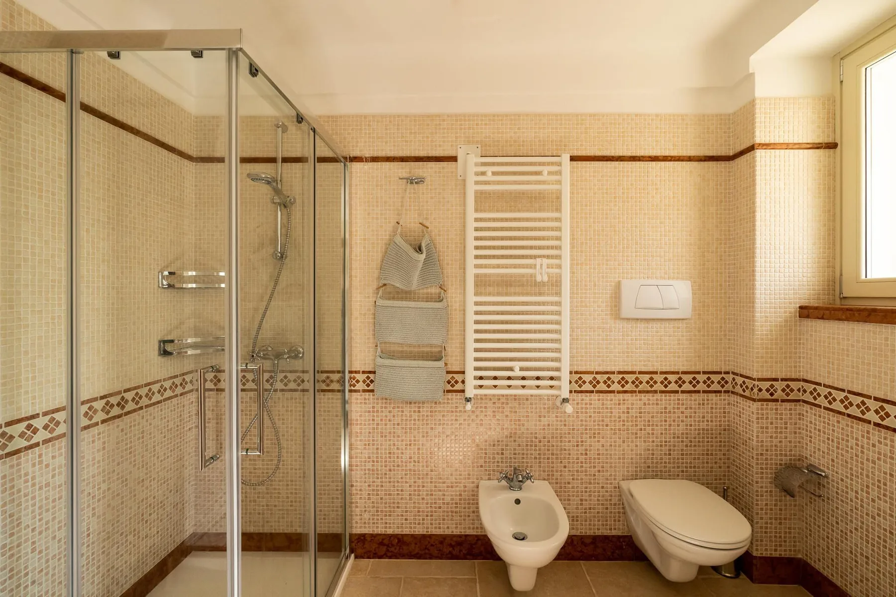 A tiled bathroom with a glass shower, wall-mounted basin, and toilet.