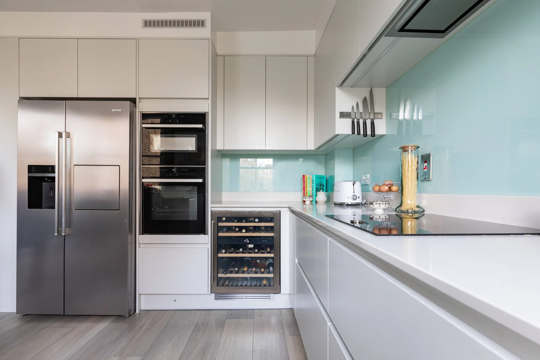A modern kitchen with white cabinetry, stainless steel appliances, and a long countertop.