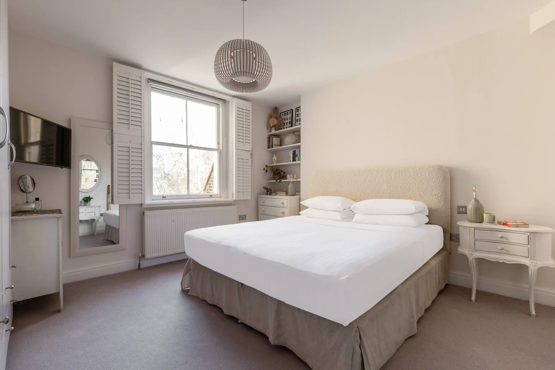 A bright bedroom with a bed beneath a large window and built-in shelving.