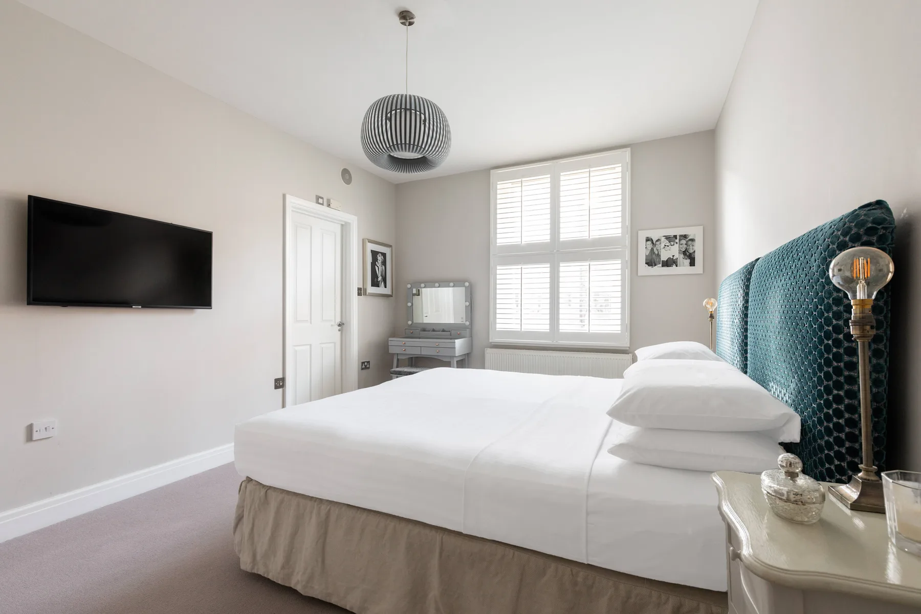 A bright bedroom with a neatly made bed and a large window with blinds.