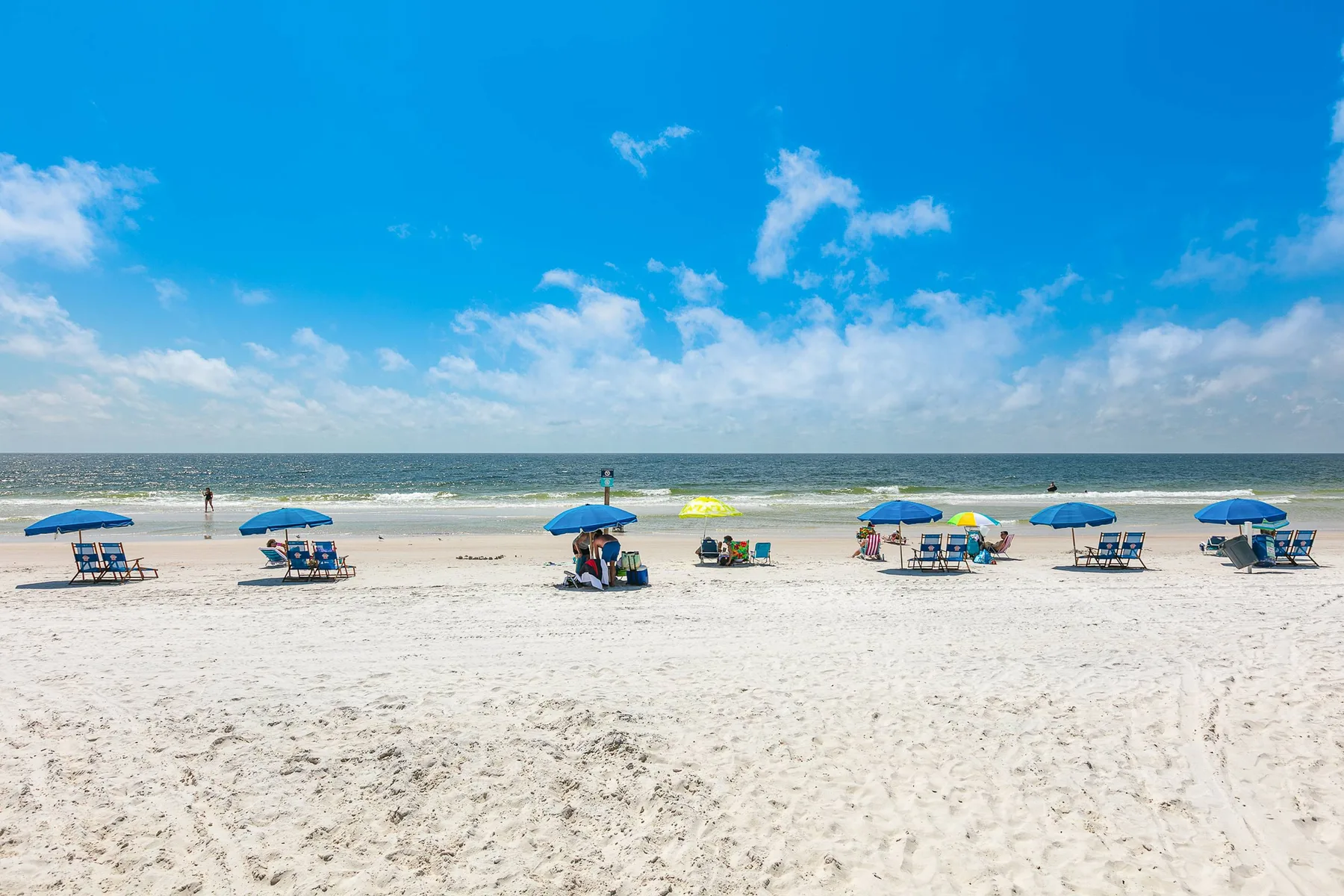 A sandy beach stretches along the ocean, with colorful umbrellas and seating.