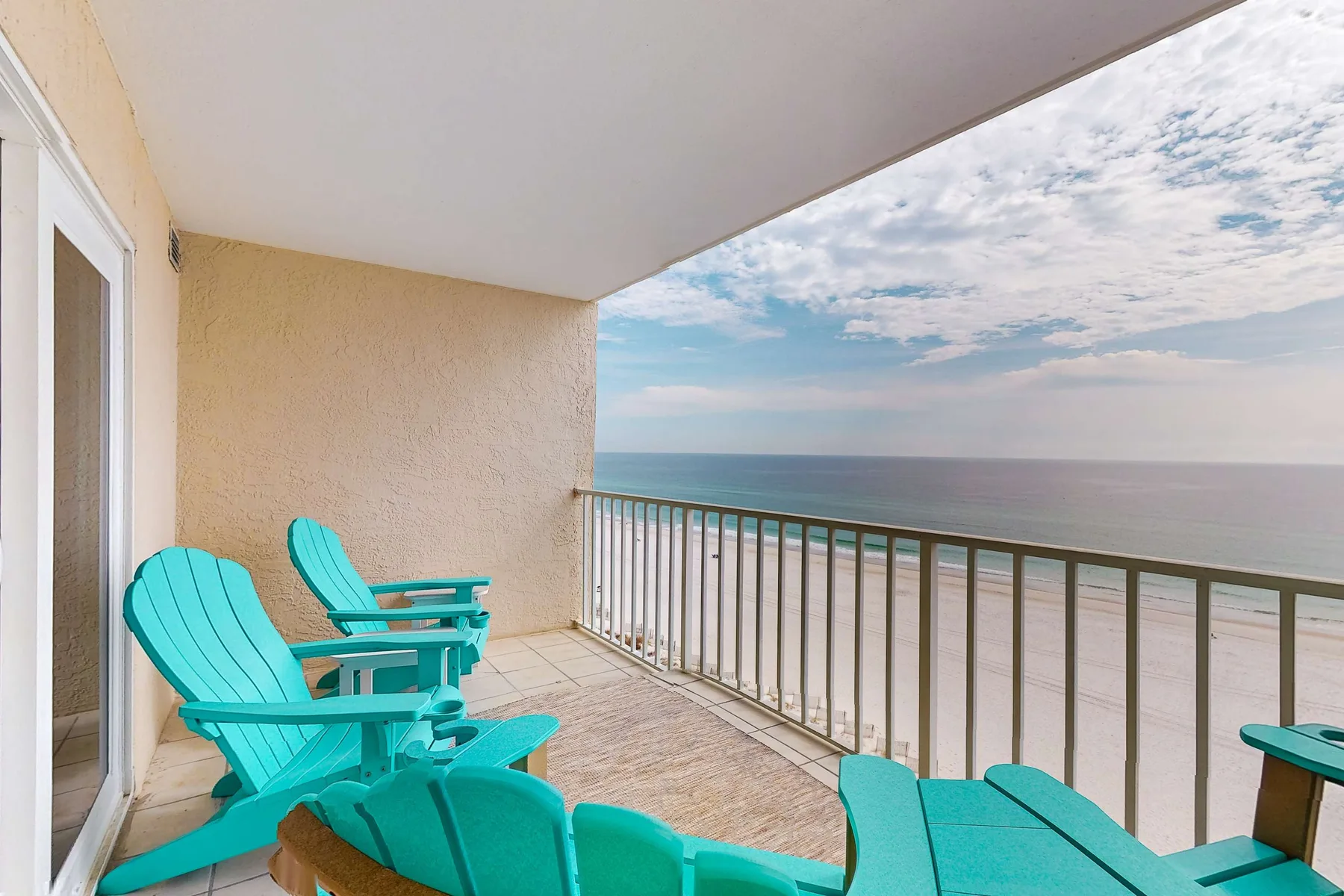 A balcony with turquoise seating overlooks the ocean beneath a partly cloudy sky.