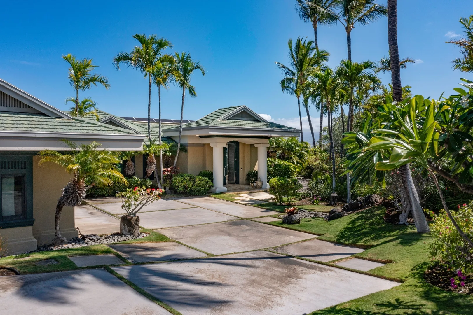 Una casa de una planta con entrada pavimentada, palmeras y vegetación tropical.