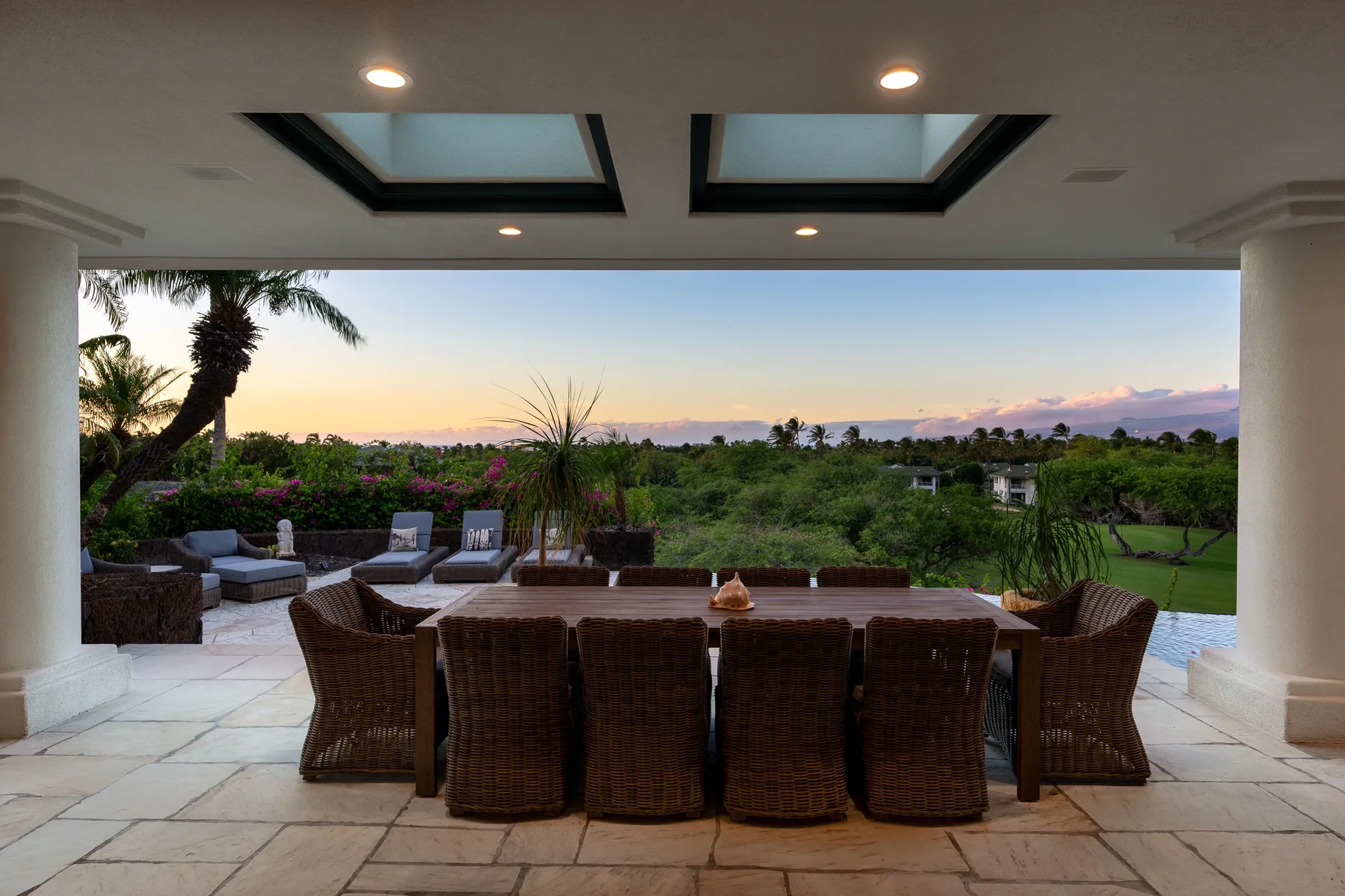 Una zona de comedor en un patio cubierto se abre a un jardín al atardecer.