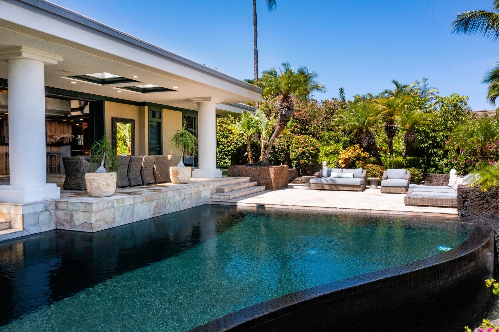 Una piscina al aire libre junto a un patio cubierto con asientos y plantas tropicales.