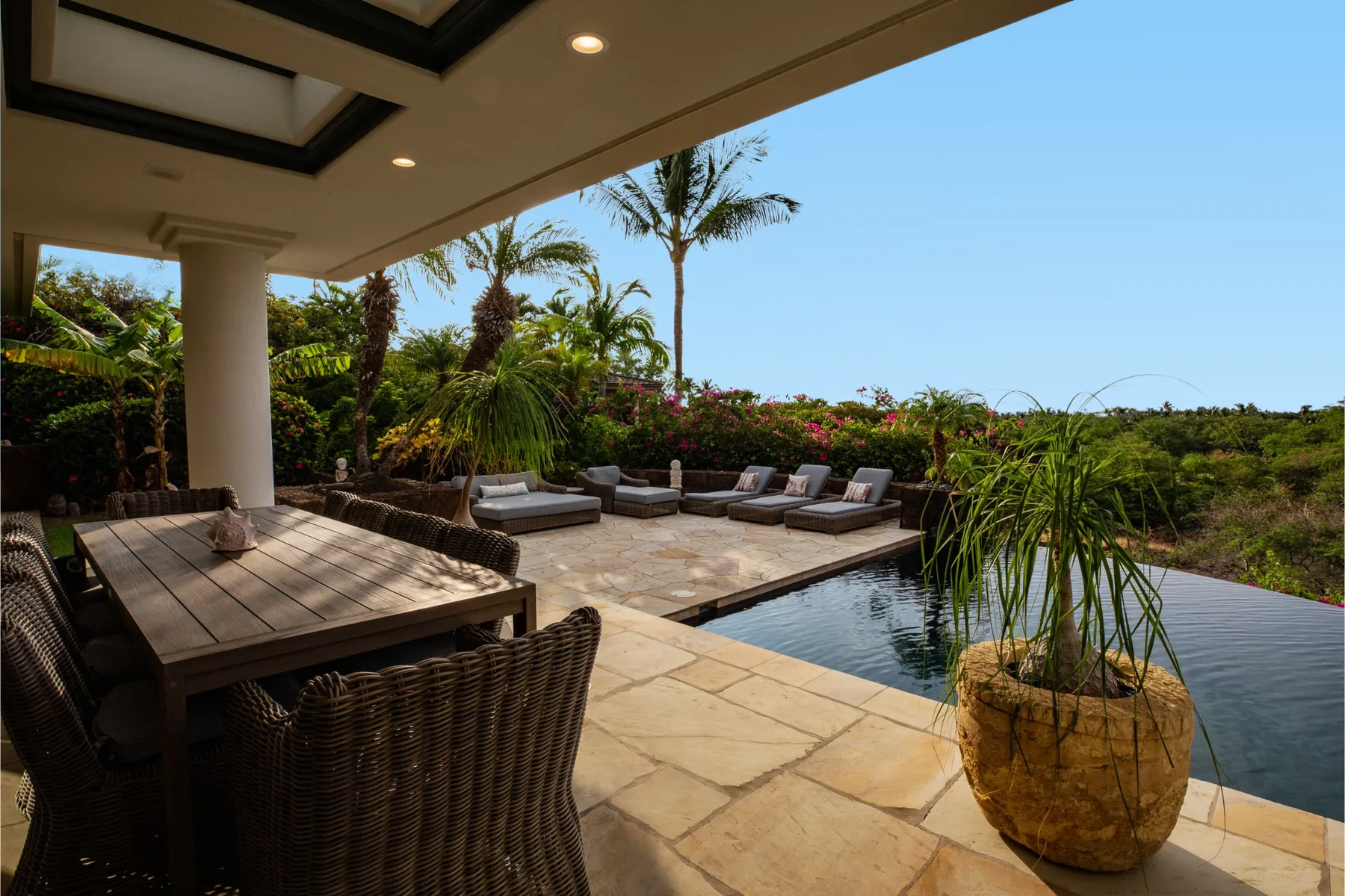Un patio cubierto con asientos al aire libre da a una piscina y un jardín tropical.