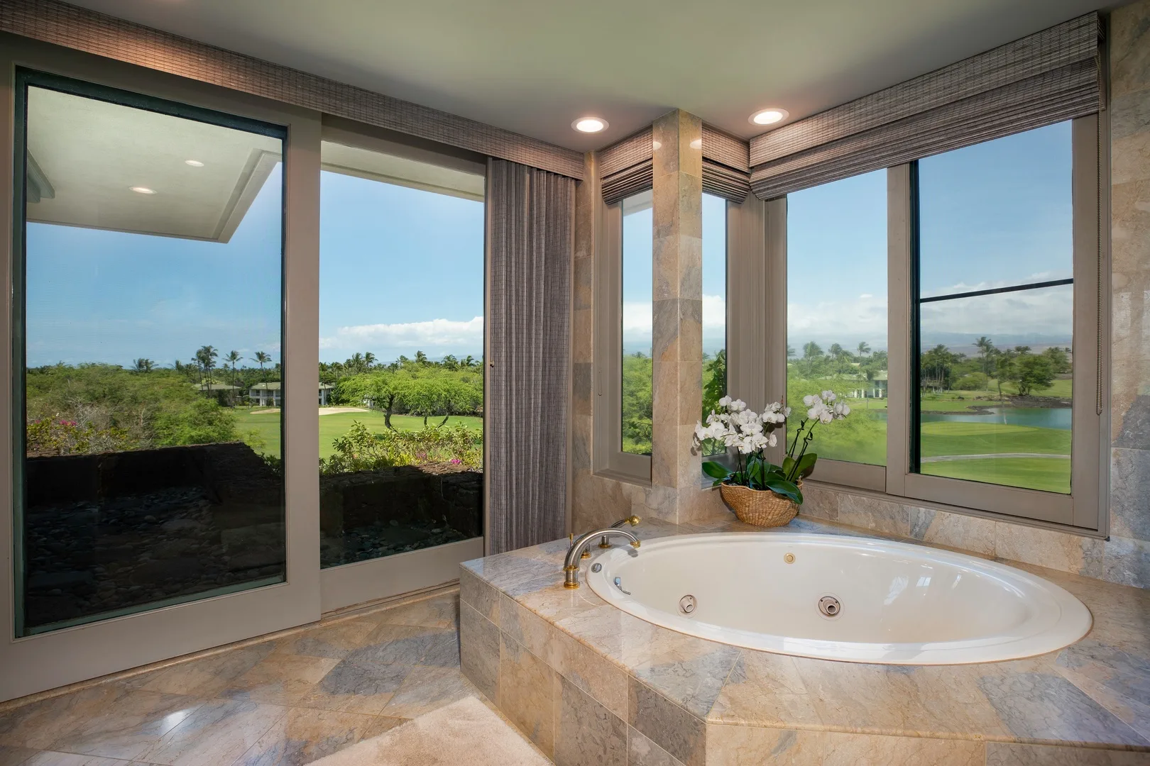 Un baño tiene una bañera empotrada junto a grandes ventanas con vista a zonas verdes.