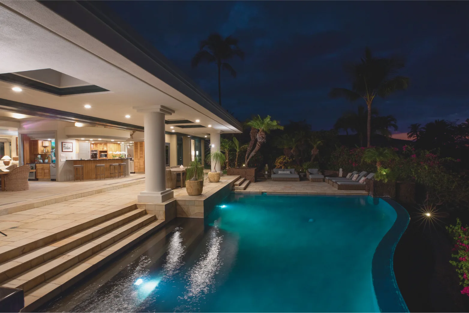 Una piscina exterior iluminada junto a un patio cubierto por la noche.