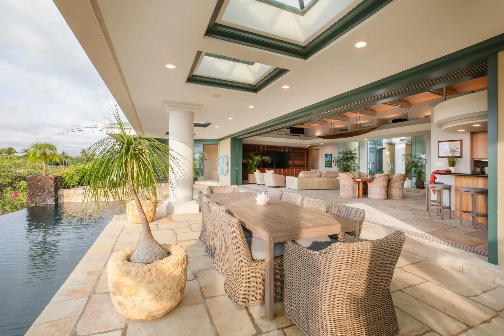 Una sala y comedor diáfanos con asientos de mimbre junto a una piscina.