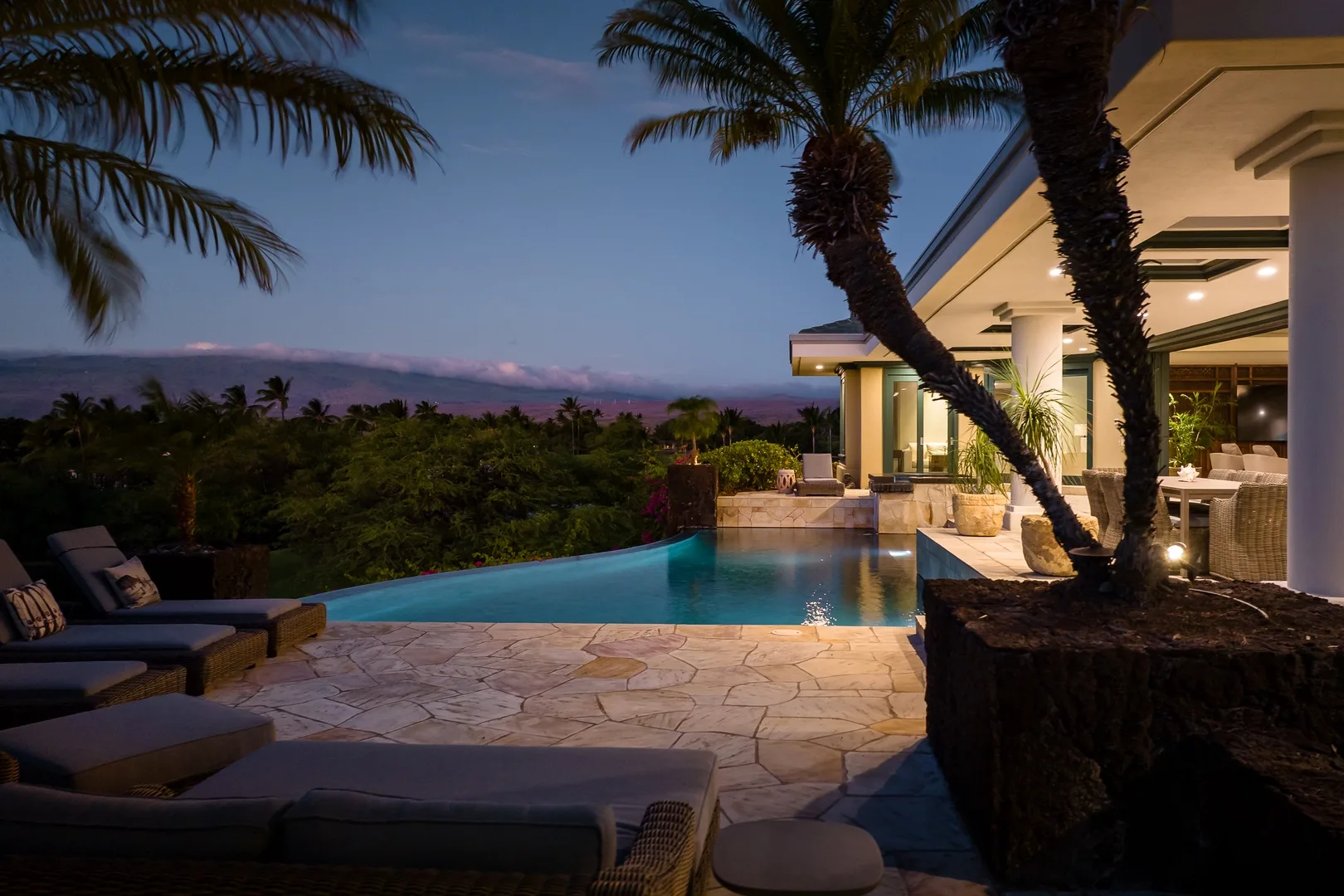 Piscina exterior junto a un patio con asientos al anochecer.