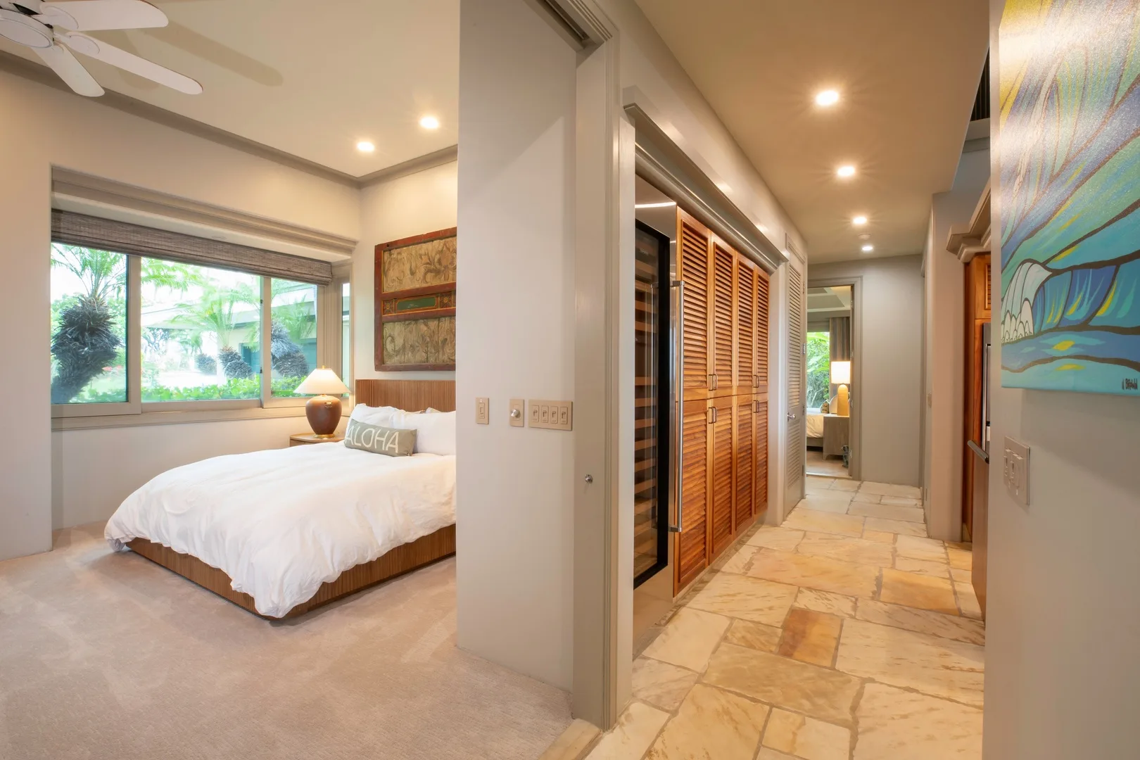 Un dormitorio con una cama junto a una ventana grande, junto a un pasillo con puertas de madera.