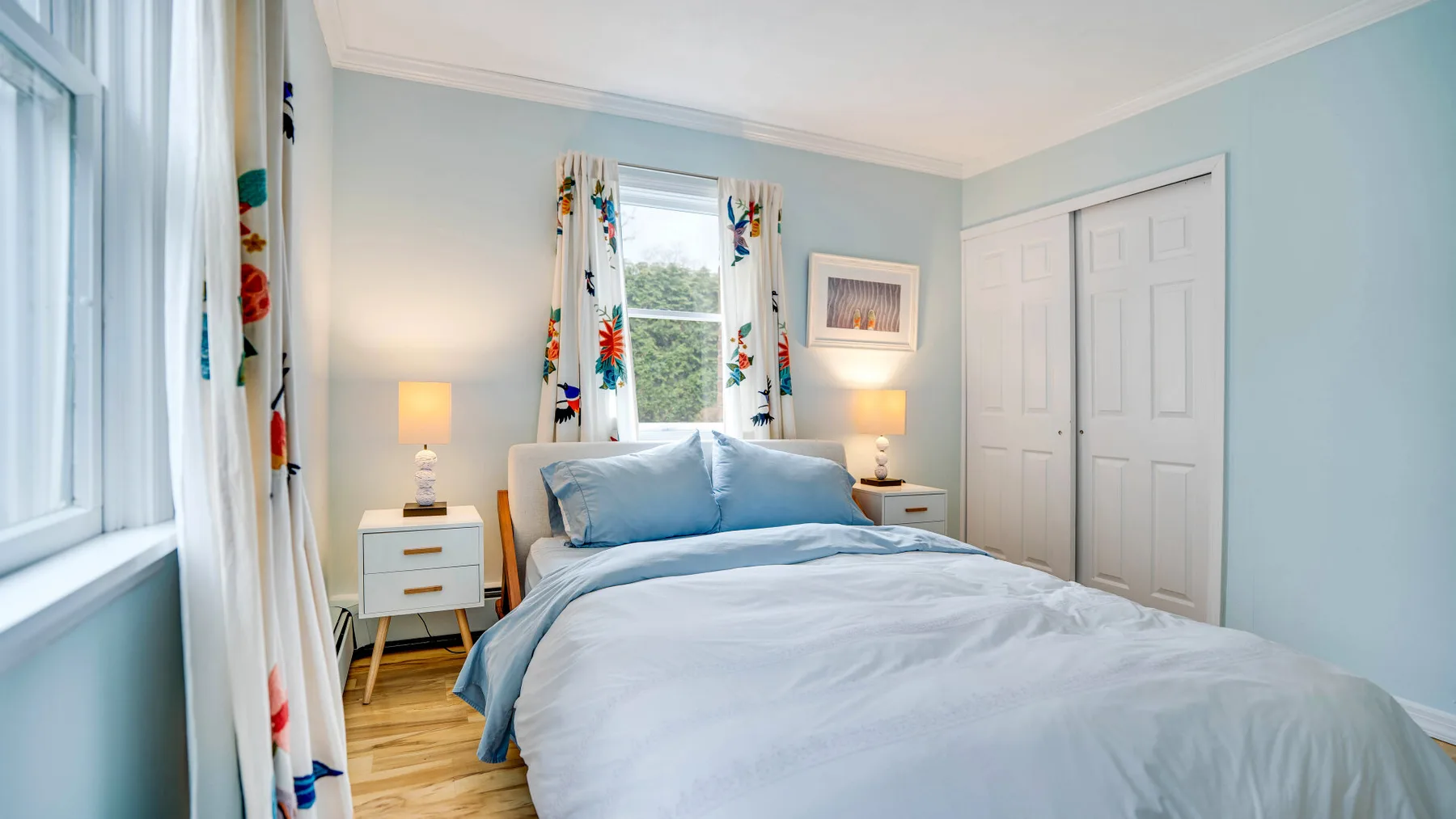 Un dormitorio con una cama bien tendida y cortinas coloridas junto a las ventanas.