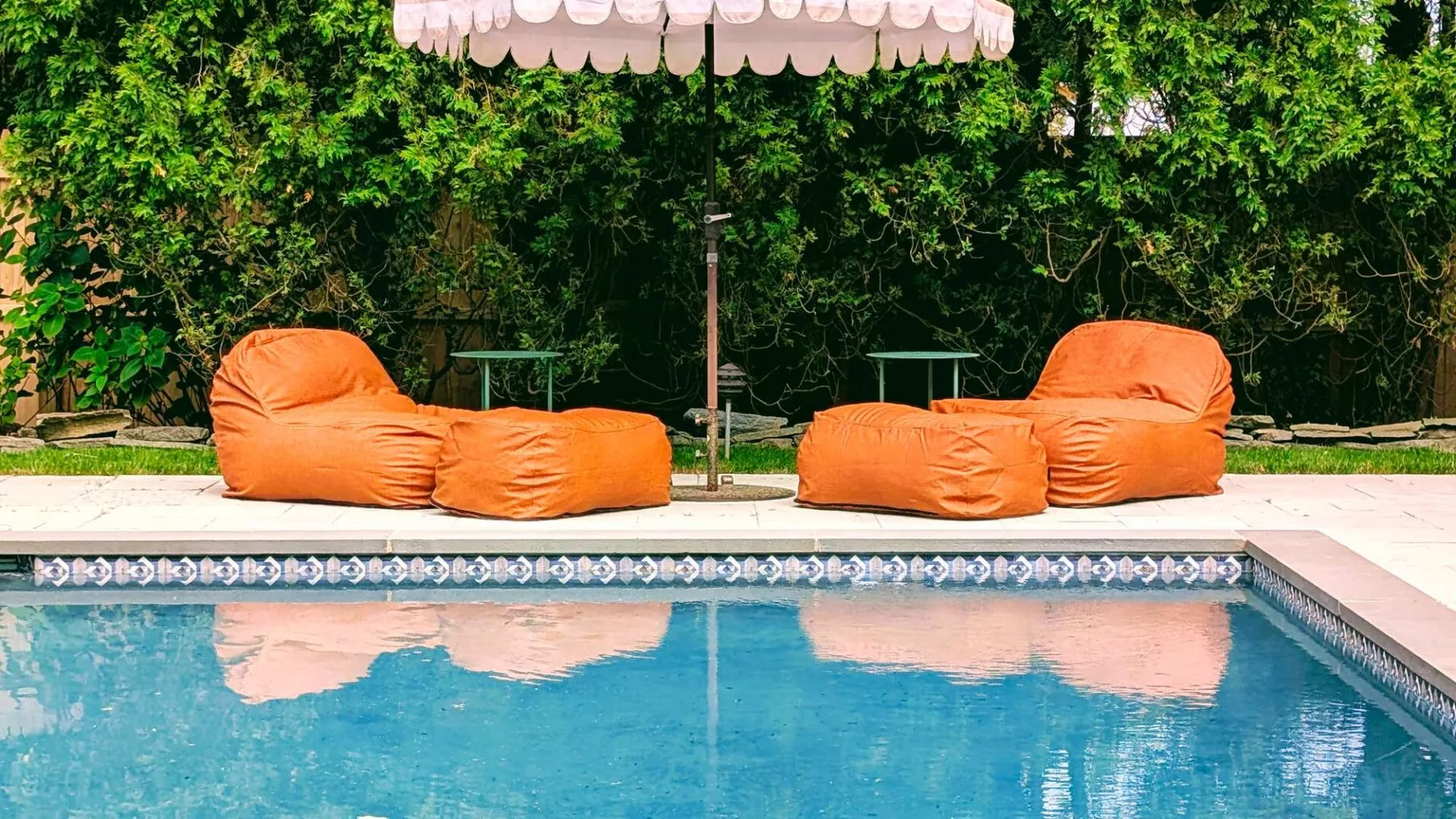 A swimming pool with orange lounge seating beneath a striped canopy.
