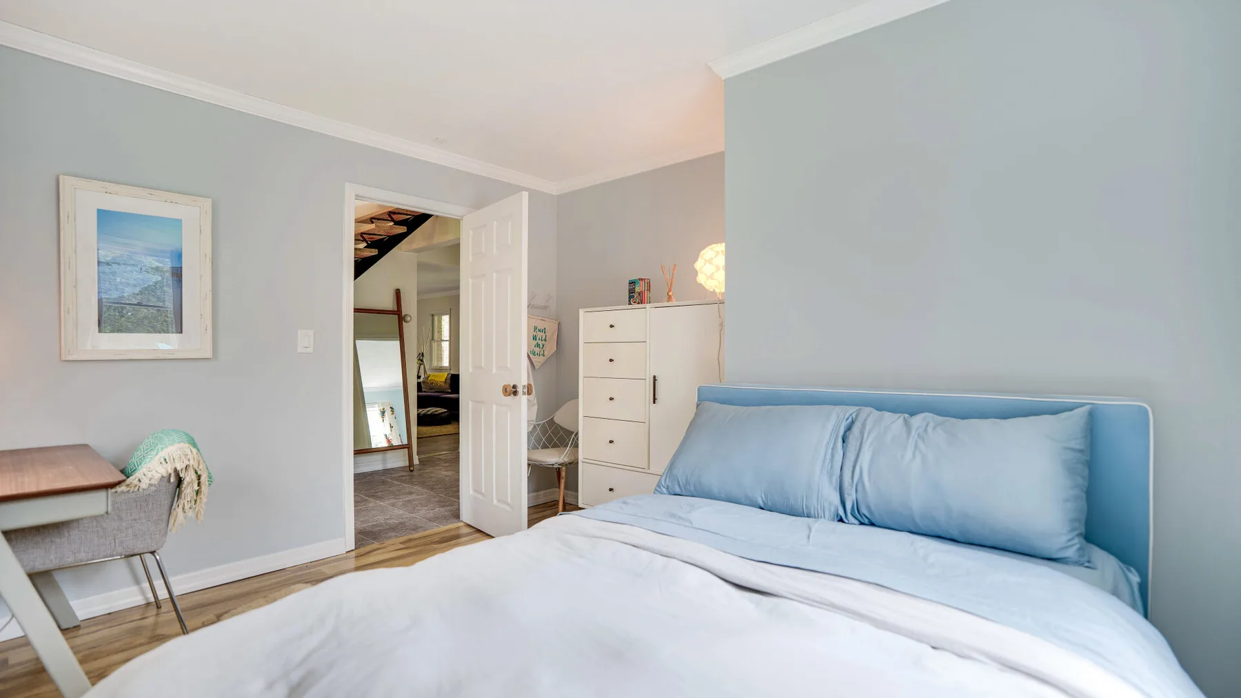 Un dormitorio con una cama vestida con ropa de cama azul claro y una puerta abierta.