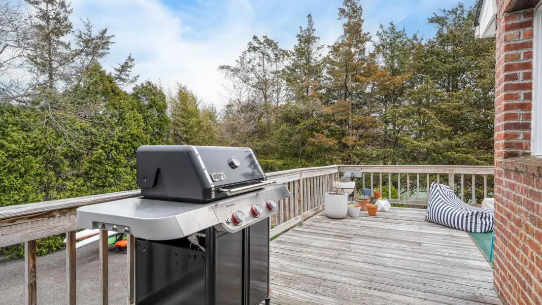 Una terraza de madera con una parrilla y asientos al aire libre, rodeada de árboles.