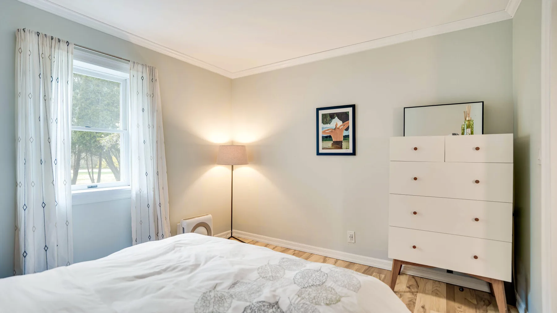 Un dormitorio con una cama junto a una ventana y una cómoda alta.