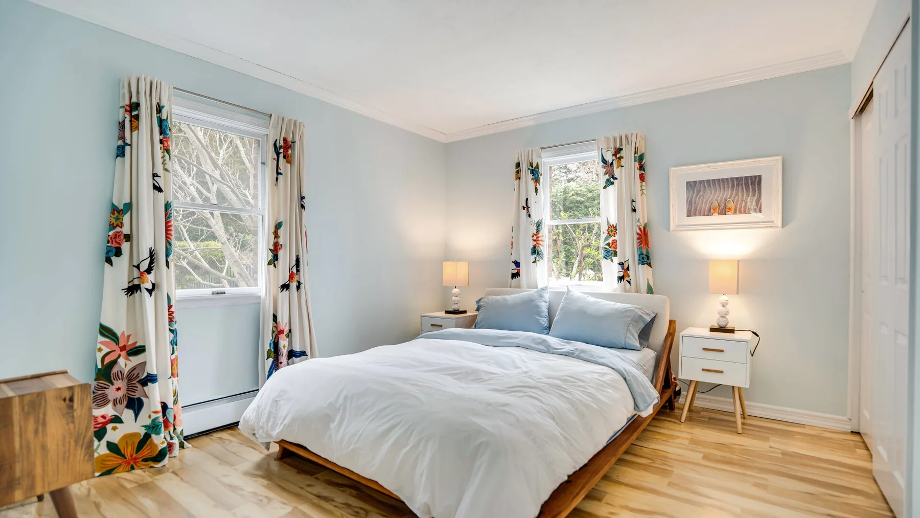 Un dormitorio con una cama, cortinas florales y paredes azul claro.