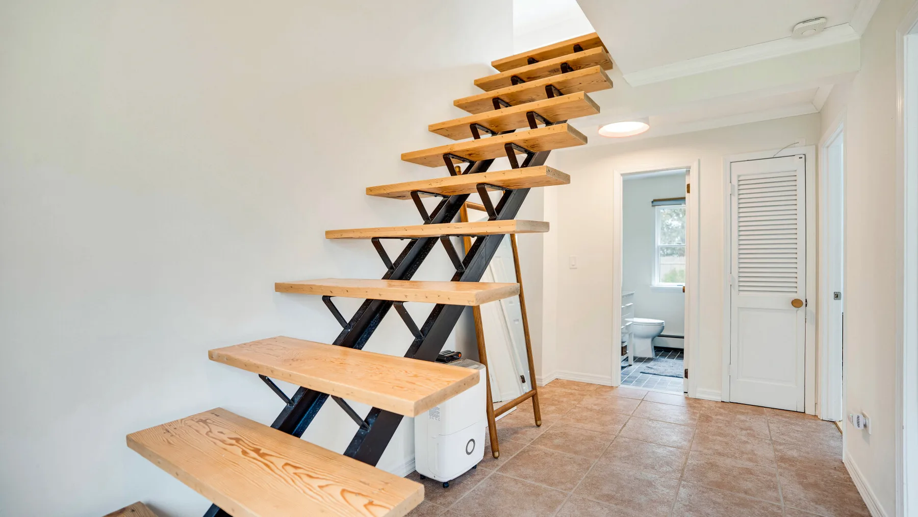 Un pasillo interior con una escalera abierta y una puerta al baño.