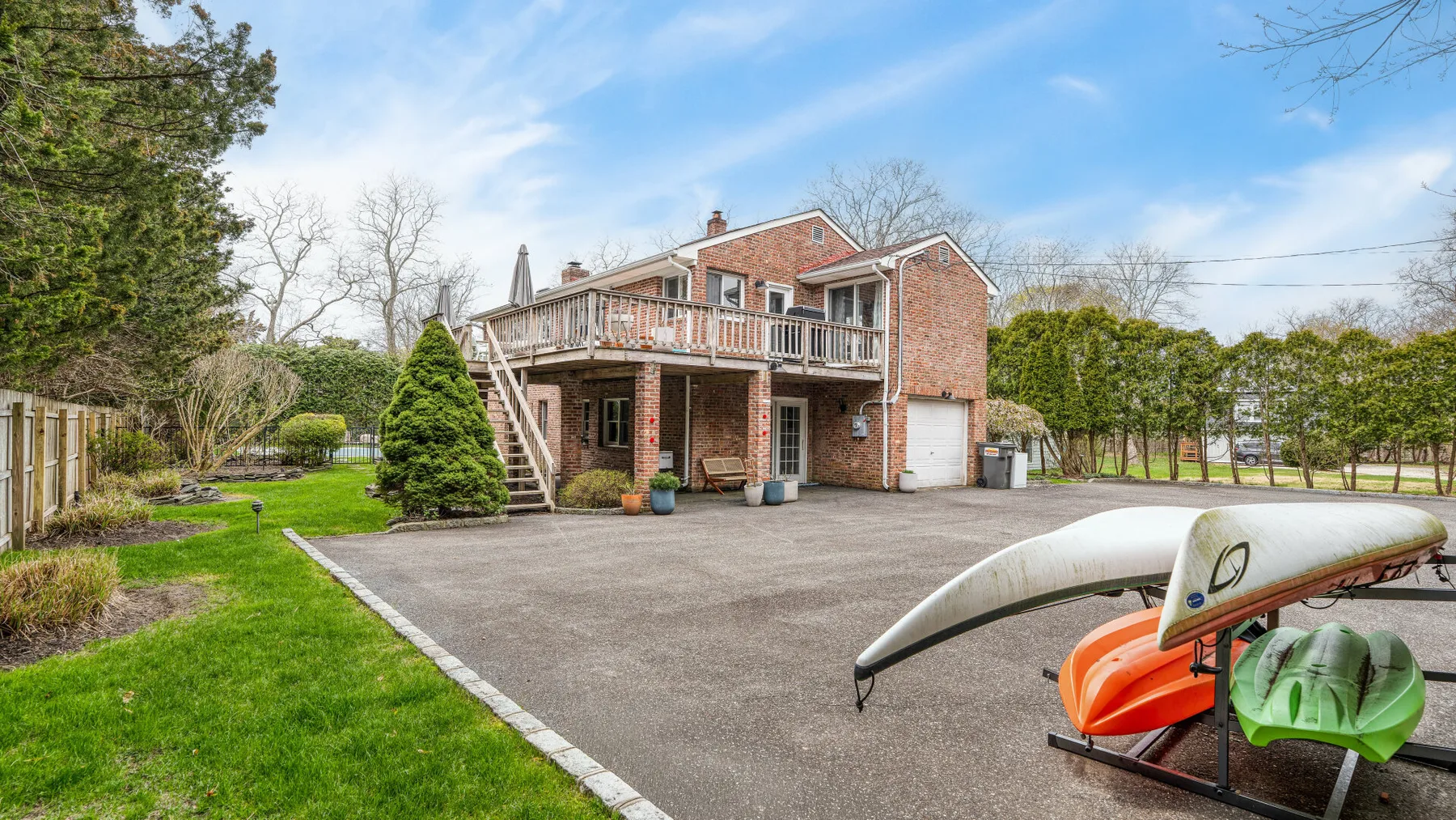 Una casa de ladrillo con terraza elevada da a un patio pavimentado con kayaks cerca.