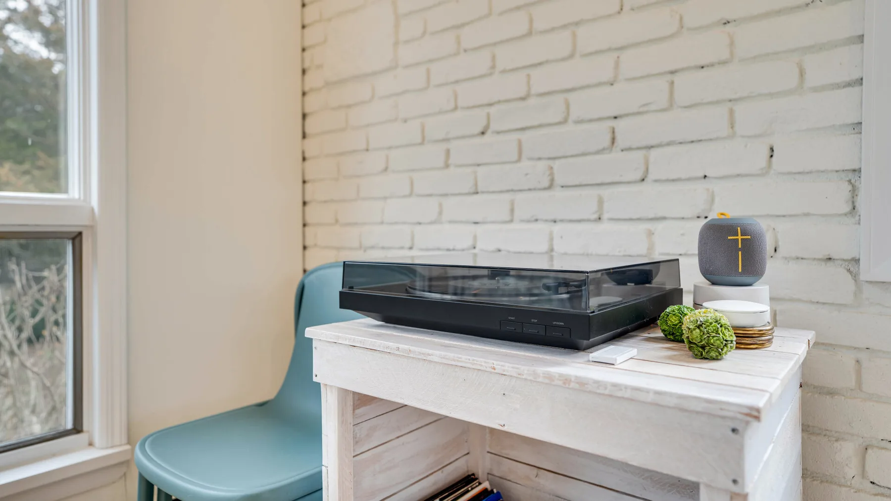Un tocadiscos está sobre una mesa blanca junto a una ventana y una pared de ladrillo blanco.