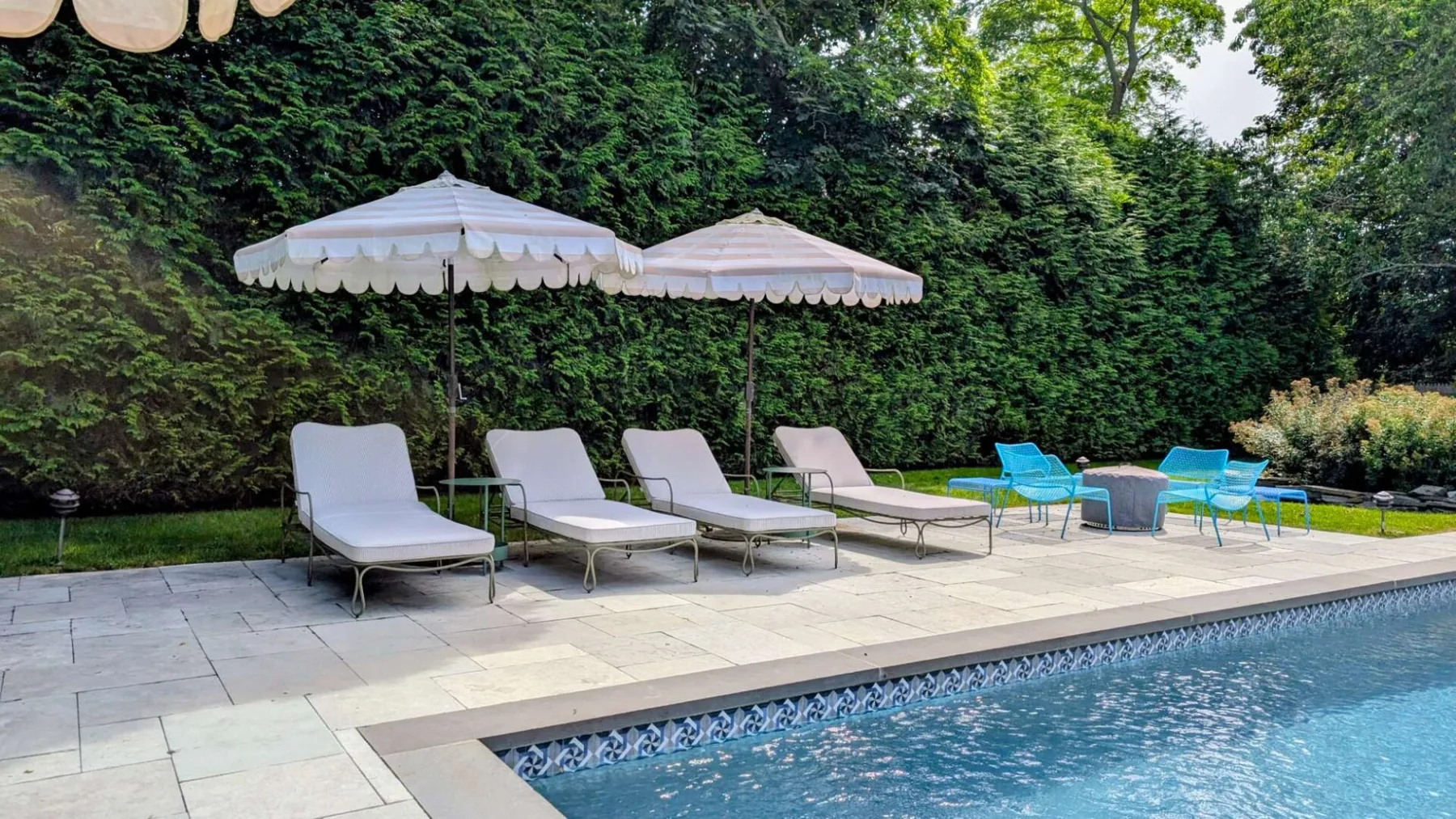 Una piscina exterior junto a un patio pavimentado con tumbonas y sombrillas.