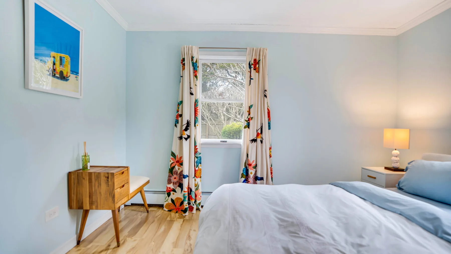Un dormitorio luminoso con una cama, una ventana y cortinas coloridas.
