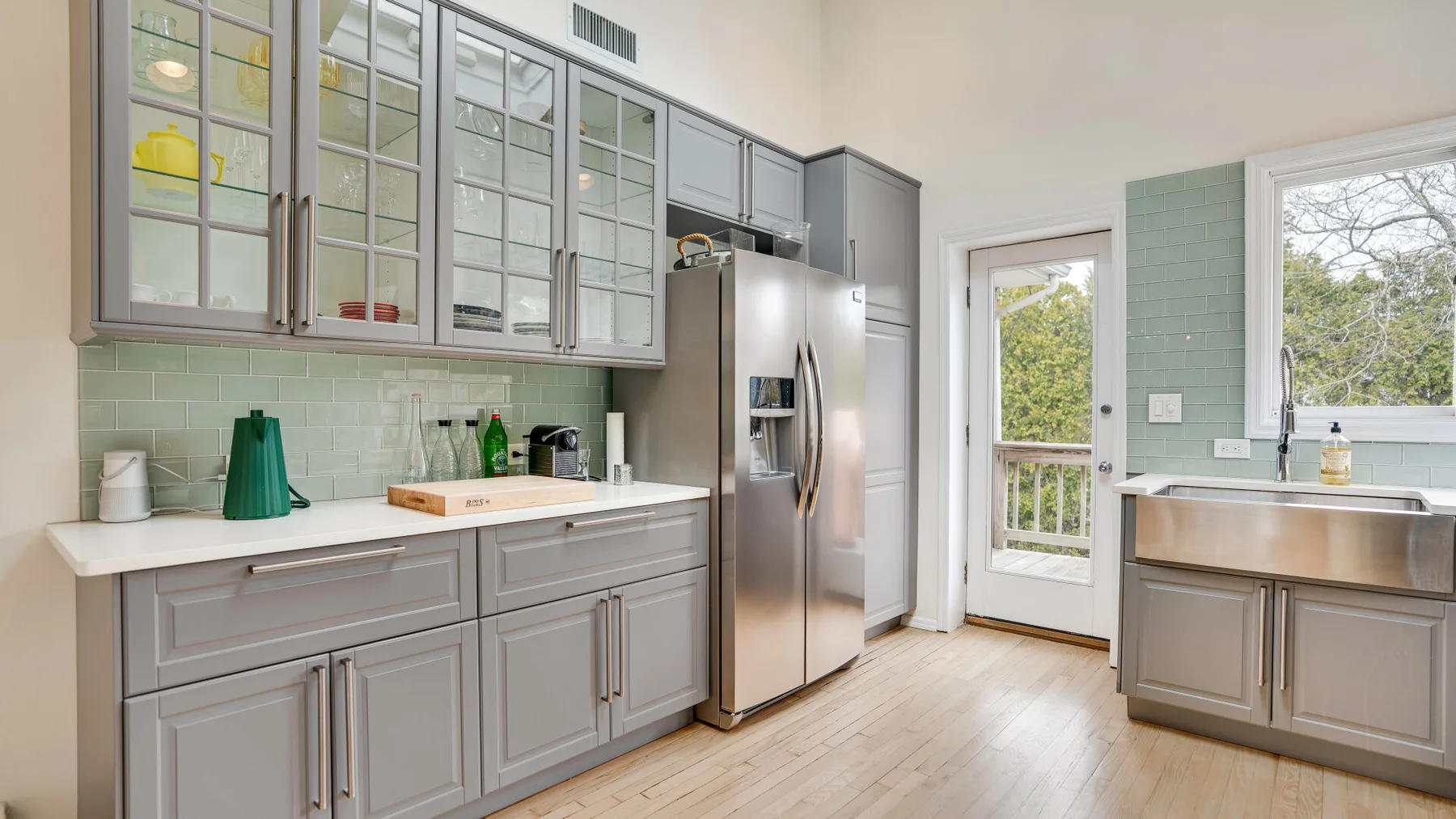 Una cocina luminosa con gabinetes grises, un refrigerador y un fregadero bajo una ventana.