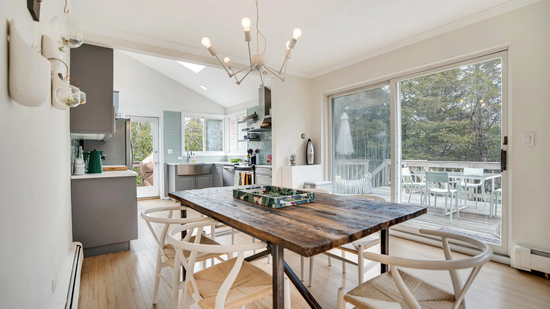Comedor luminoso con una mesa de madera junto a grandes ventanas y puertas corredizas de vidrio.