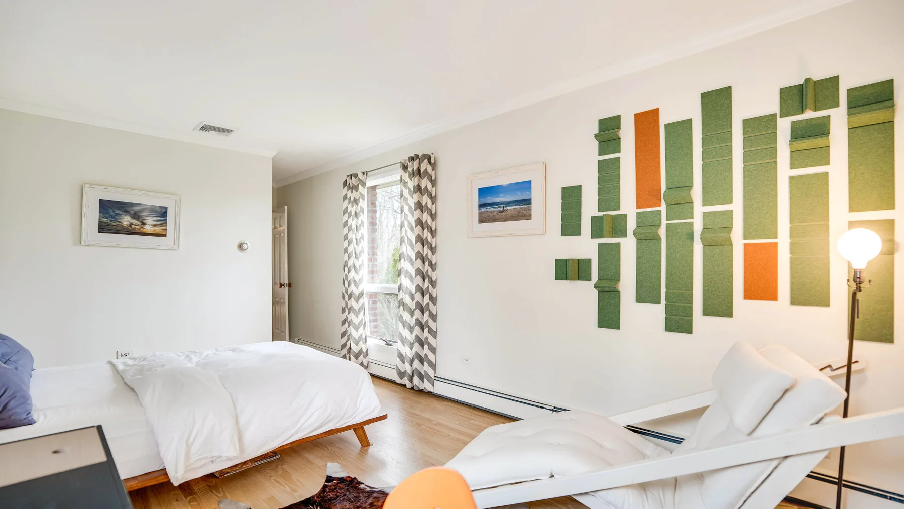 Un dormitorio luminoso con ropa de cama blanca y arte colorido en la pared.