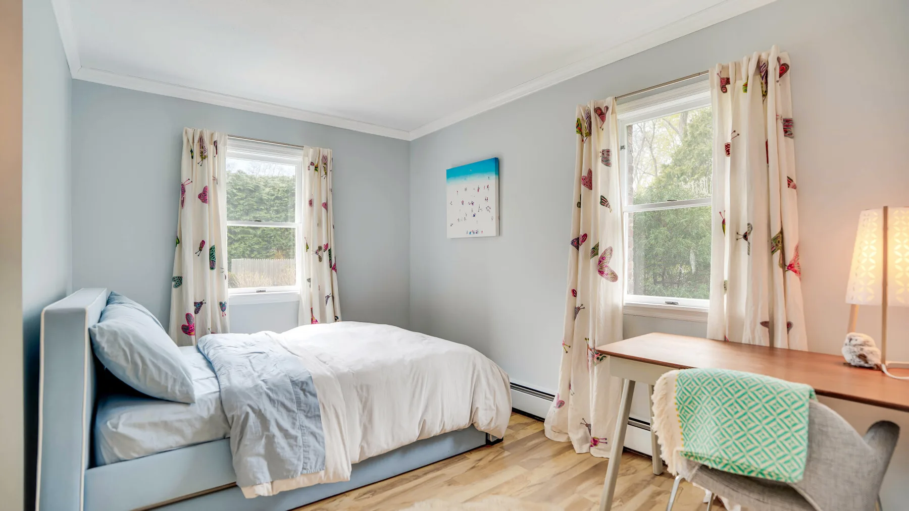 Un dormitorio con una cama junto a dos ventanas y un escritorio pequeño.