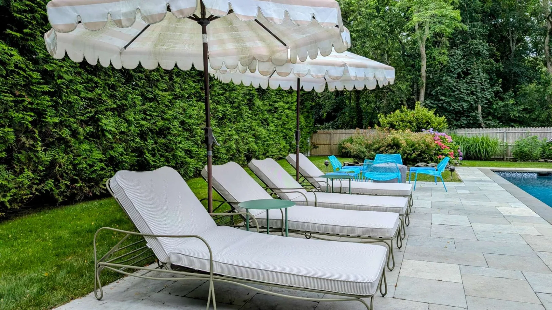 Asientos junto a la piscina al aire libre bajo sombrillas blancas, junto a un jardín.