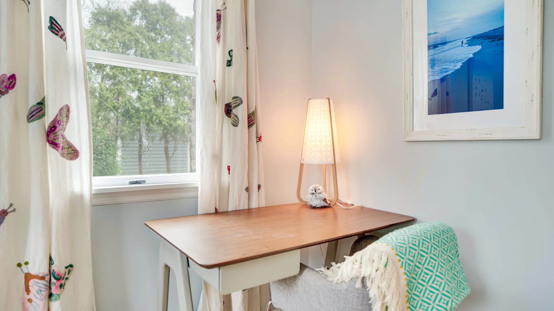 Un escritorio está junto a una ventana, con una lámpara encendida y un asiento cubierto con telas.