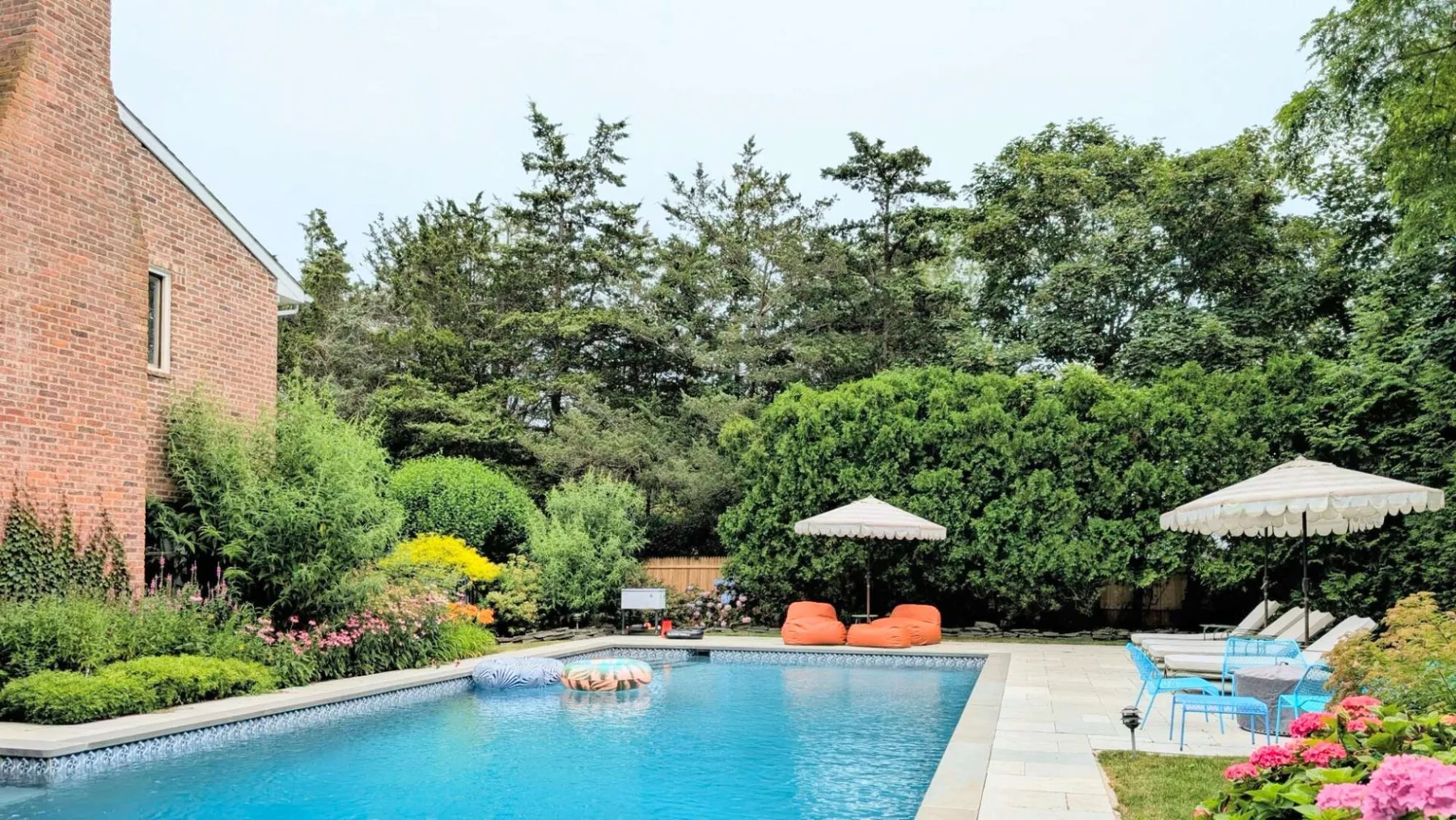 Una piscina al aire libre está rodeada de vegetación, con asientos y sombrillas junto a la terraza.