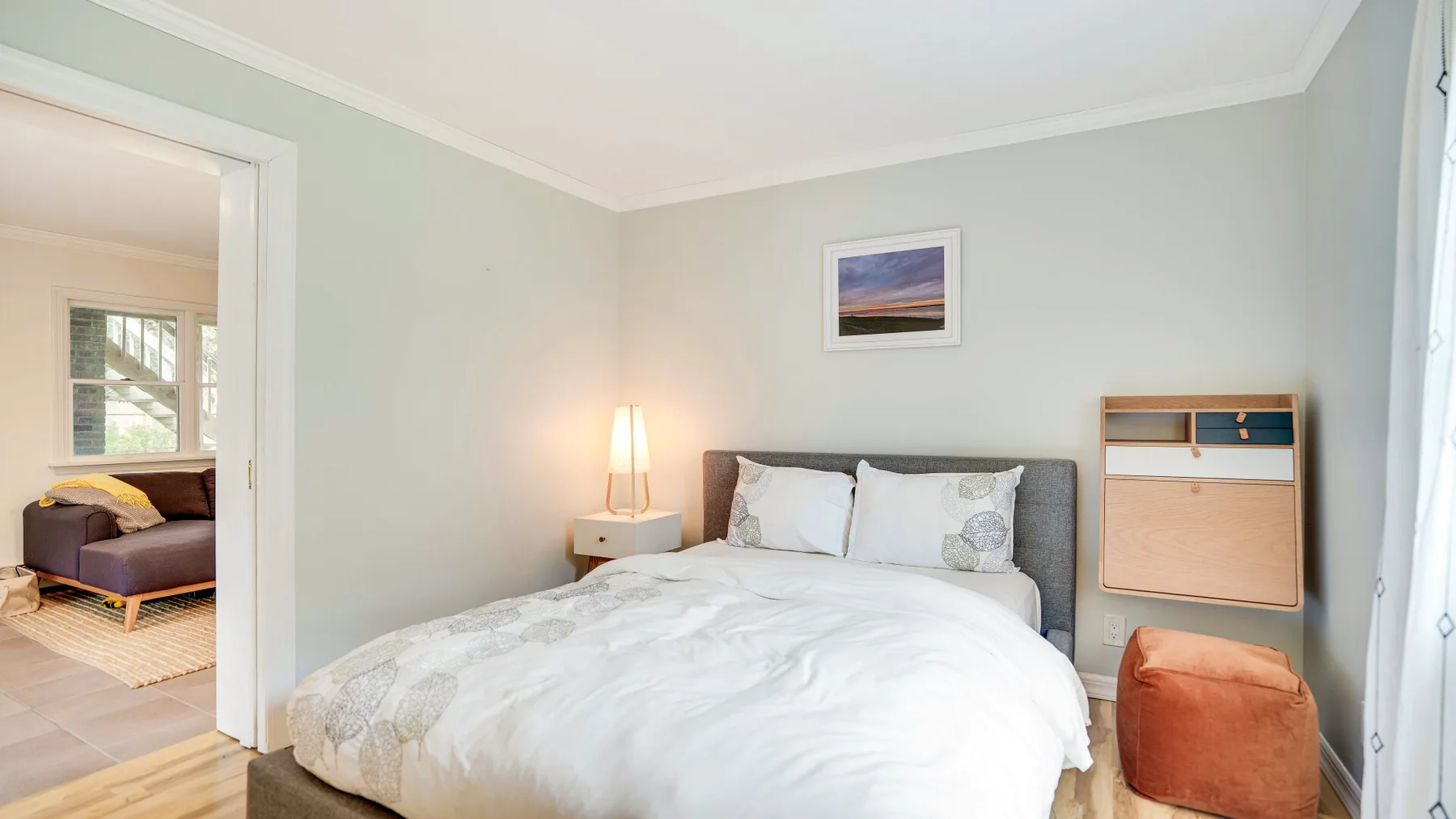 Un dormitorio luminoso con una cama grande, una mesita de noche y una cómoda pequeña.