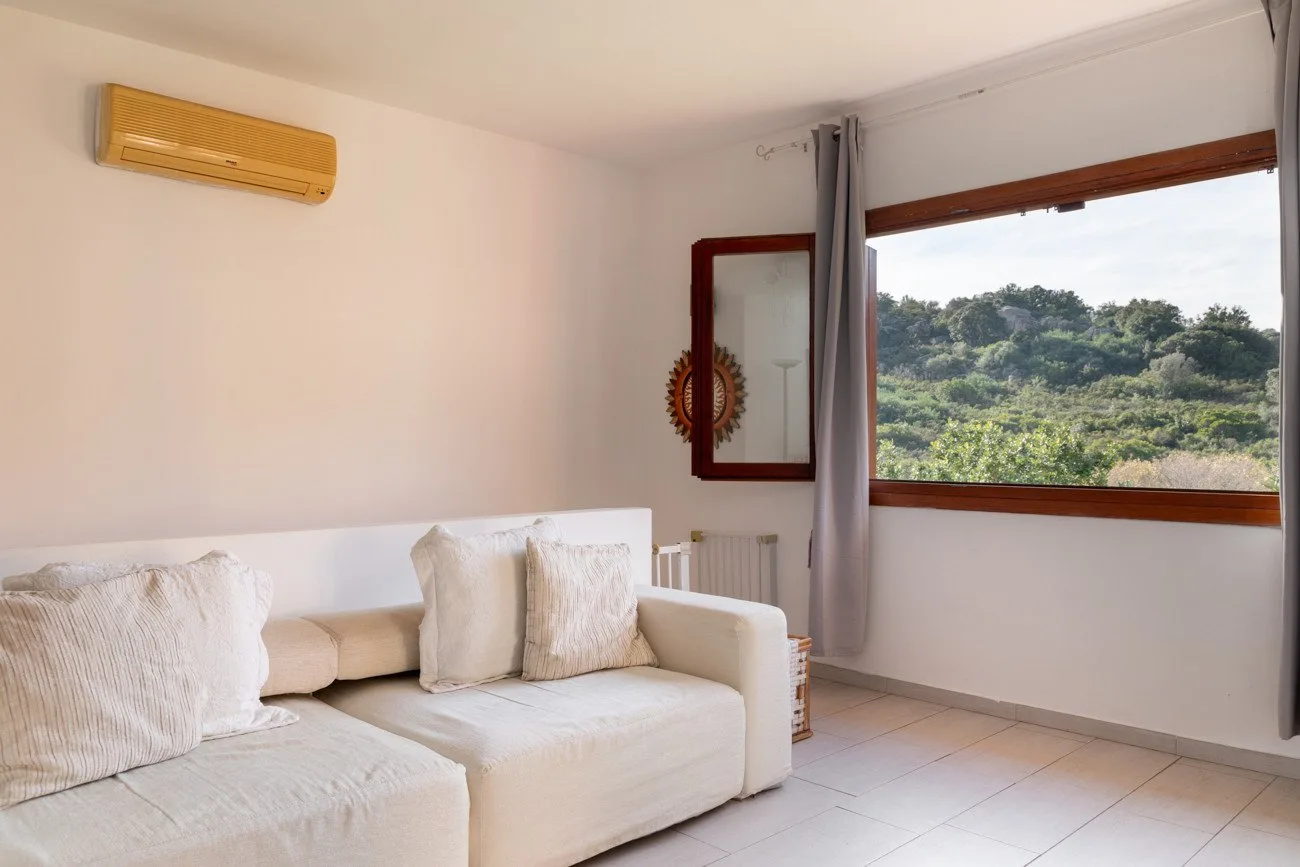 A bright living room with light seating and a large window overlooking greenery.