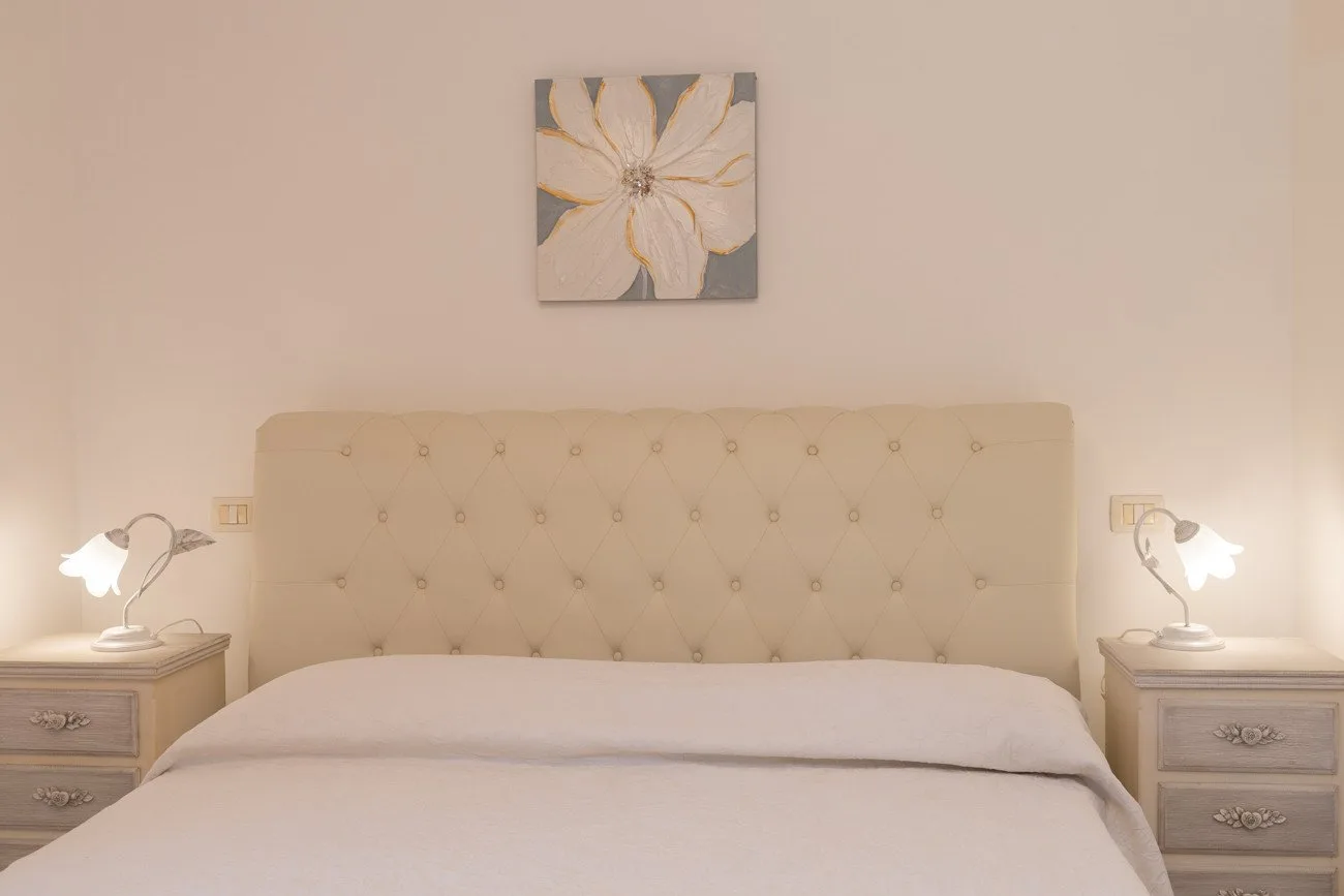 A bedroom with a bed, matching bedside tables, and a flower painting above the headboard.