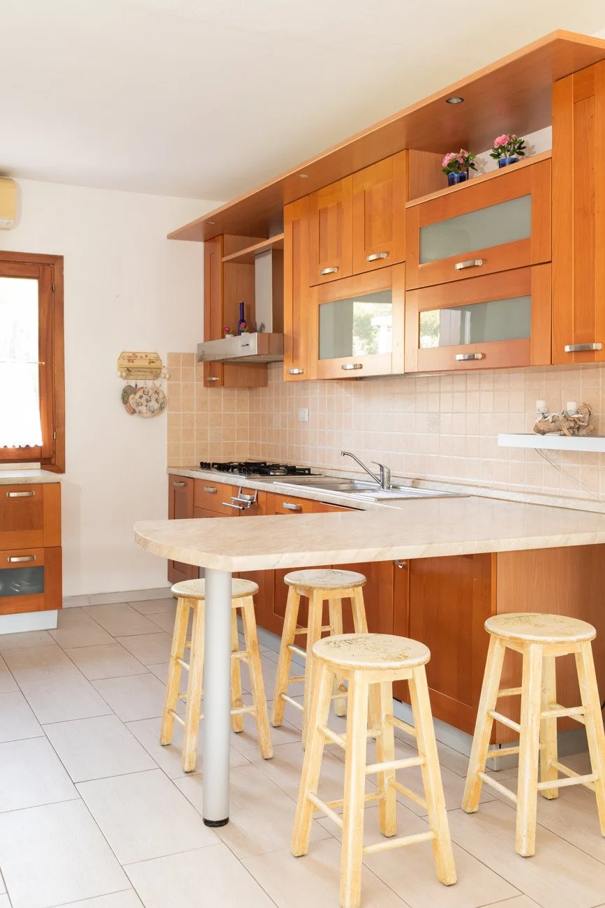 A kitchen with wooden cabinets, a tiled backsplash, and a curved counter with stools.