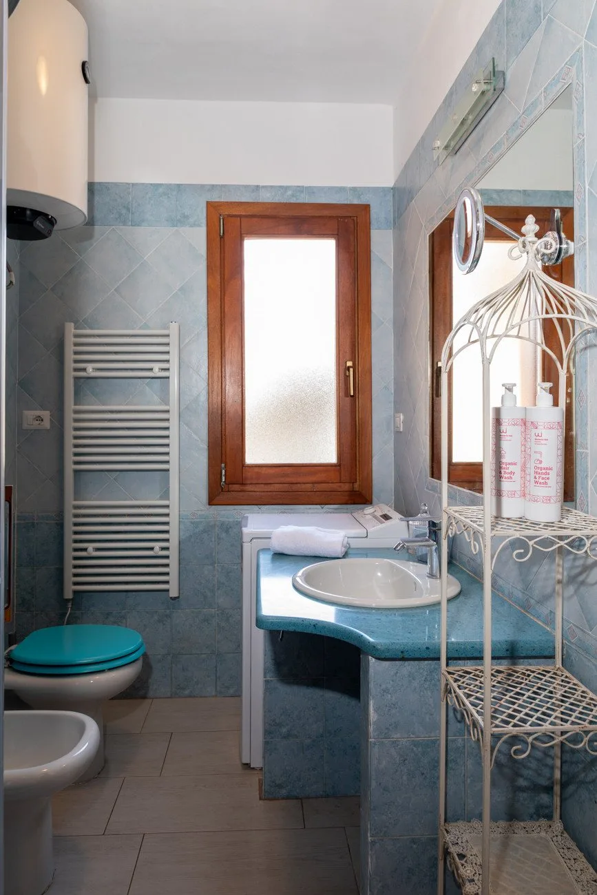 A tiled bathroom with a sink, toilet, and frosted-glass window.