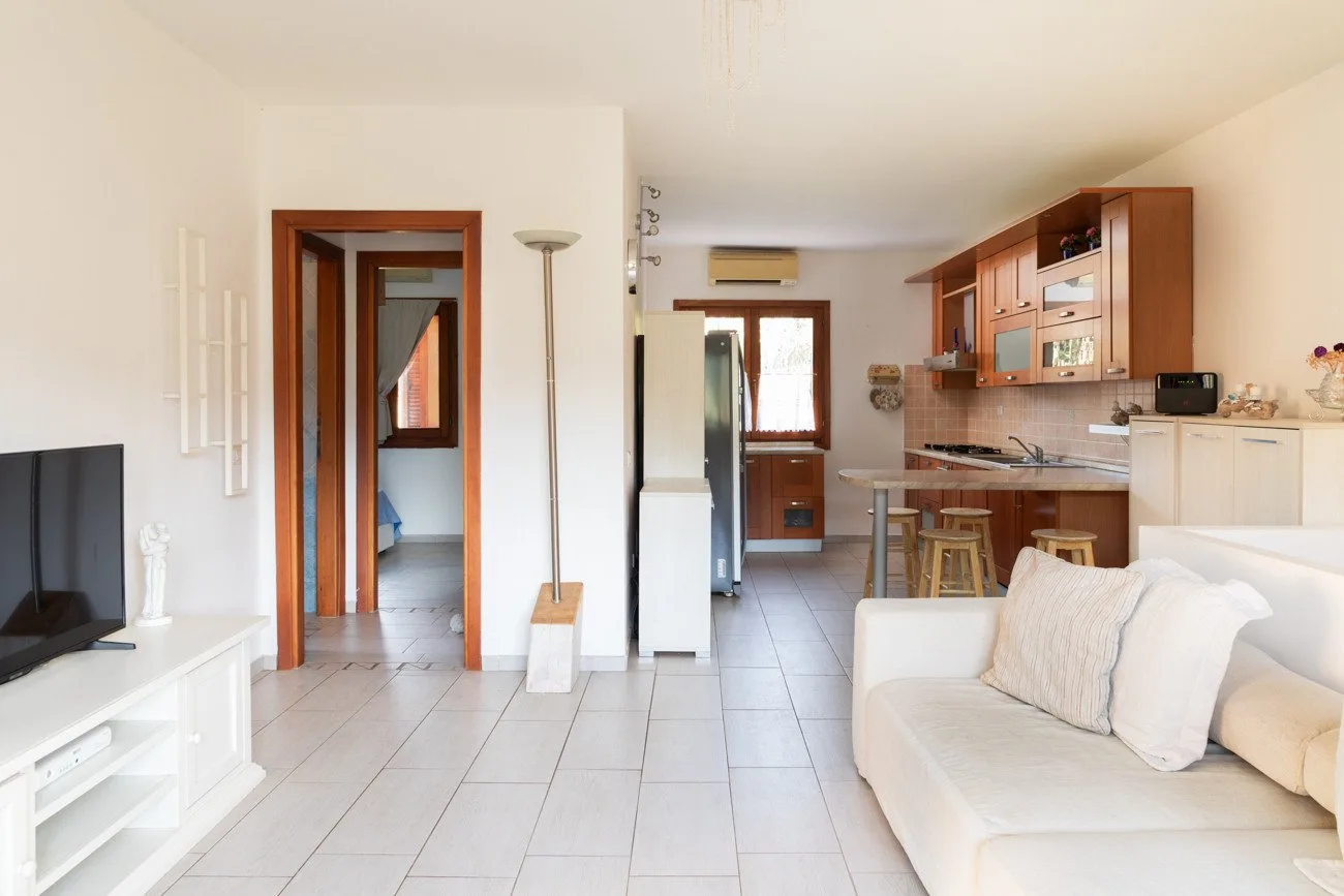 A bright living room opens into a kitchen, with a white sofa and television.