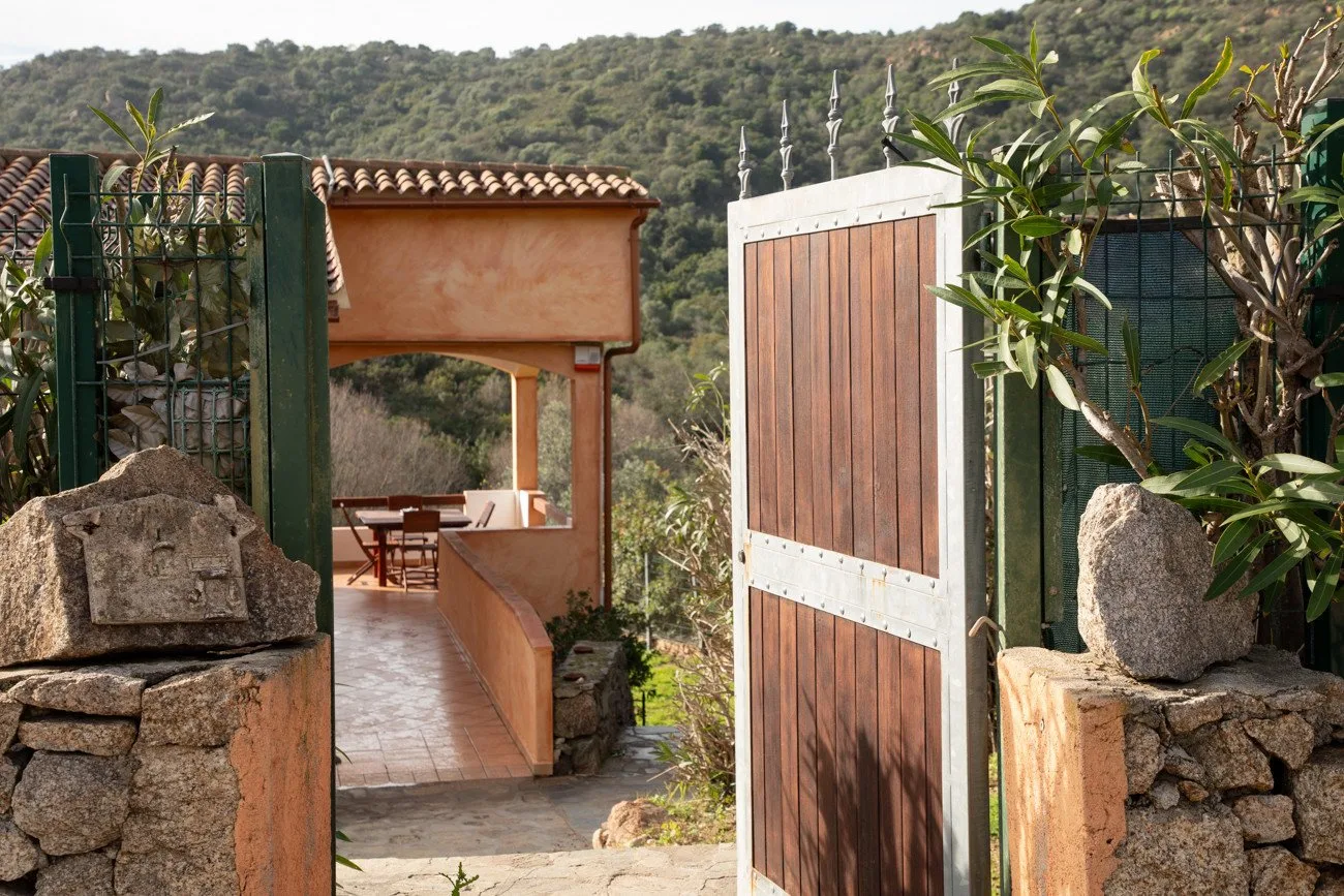 A tiled walkway passes through an open wooden gate toward a covered outdoor seating area.
